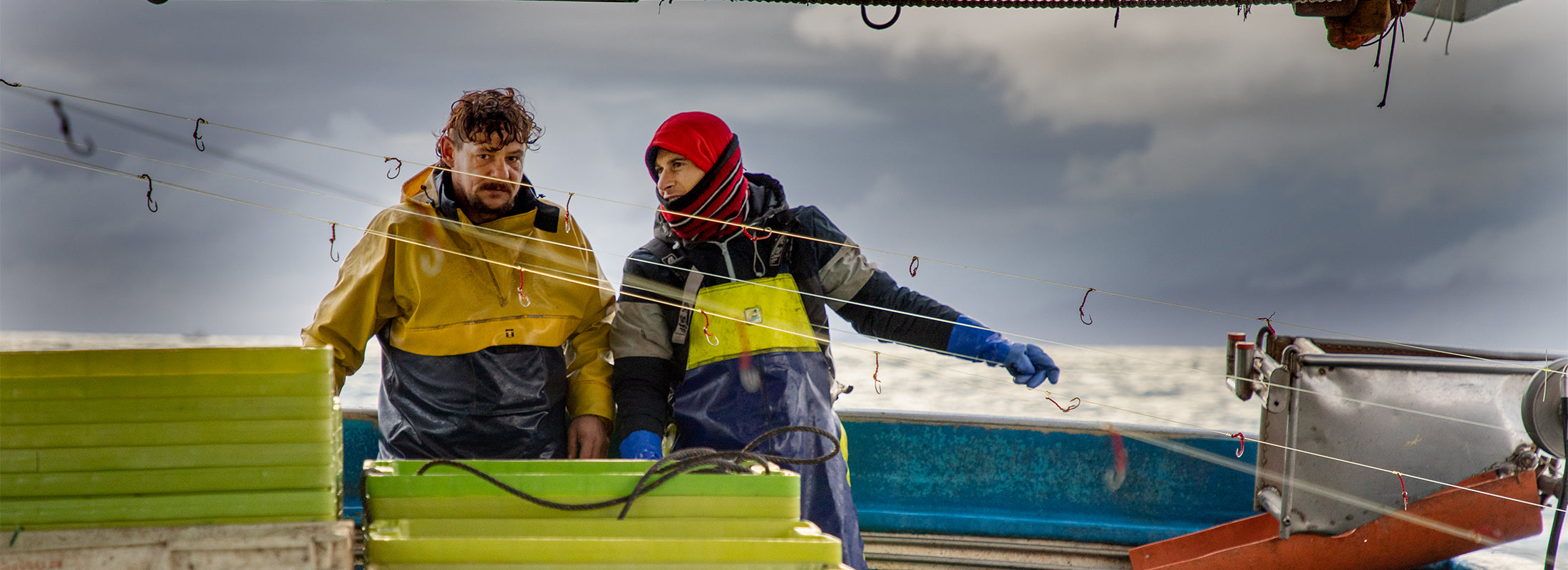 Two workers talk amongst fishing lines and boxes aboard a mackerel fishing boat